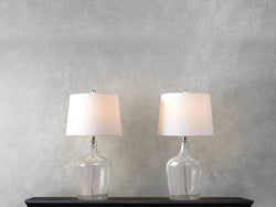 Two elegant clear glass table lamps positioned on a stylish table, illuminating the surrounding space with soft light