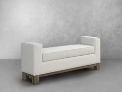 A white bench featuring wooden legs and a soft white cushion, set against a neutral background