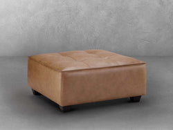 A square tan leather ottoman, showcasing a sleek and modern design, perfect for any living space